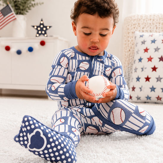 Child wearing blue pajamas with baseball pattern, sitting on a white floor.