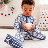 Child wearing blue pajamas with baseball pattern, sitting on a white floor.