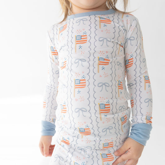 Child wearing a long-sleeve pajama top with a pattern of stars, stripes, and bows on a white background.