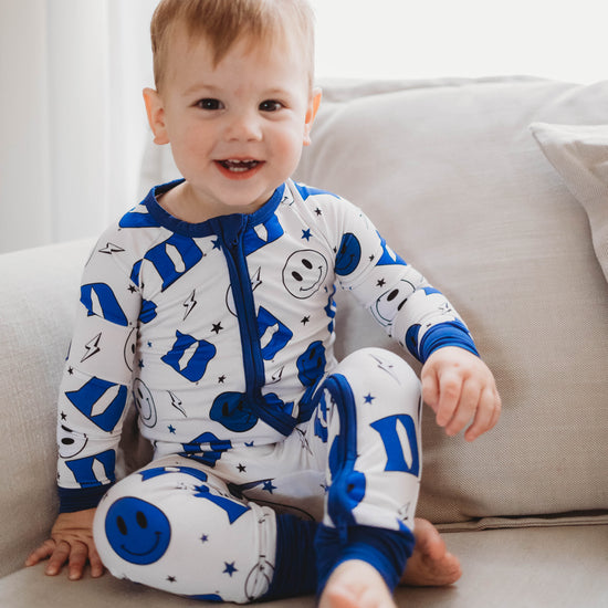 A baby in a blue and white Duke University themed romper with smiley face and logo patterns.