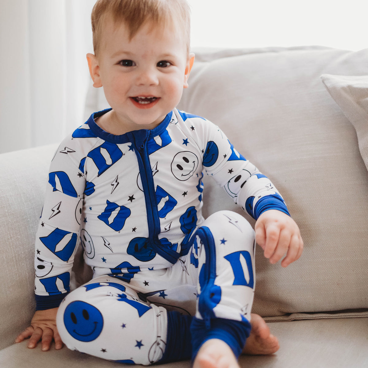 A baby in a blue and white Duke University themed romper with smiley face and logo patterns.