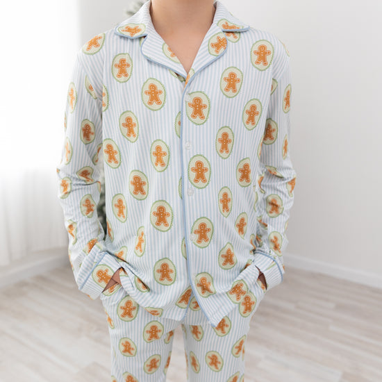 Boy wearing a light blue and white striped long sleeve pajamas with gingerbread man repeated print.