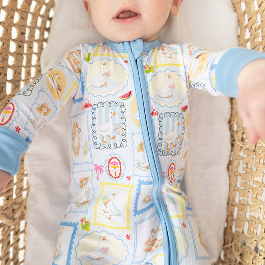 Baby wearing a blue and white patterned zippy romper with a blue zipper featuring silly gooses in a beach theme with watermelon and palm tree.