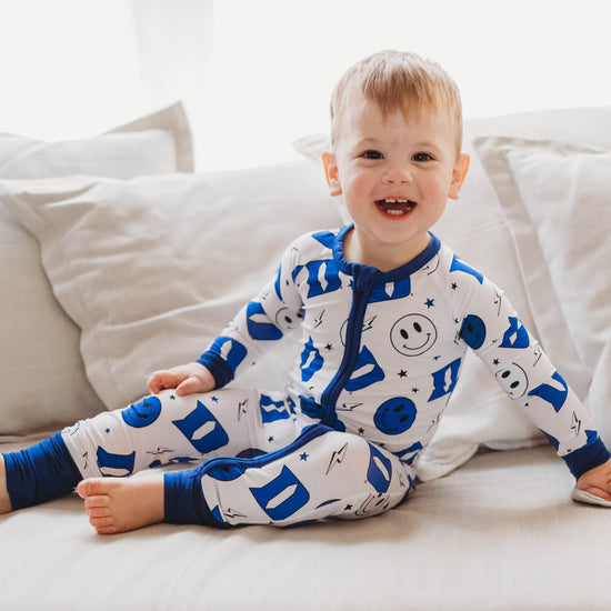 A baby in a blue and white Duke University themed romper with smiley face and logo patterns.