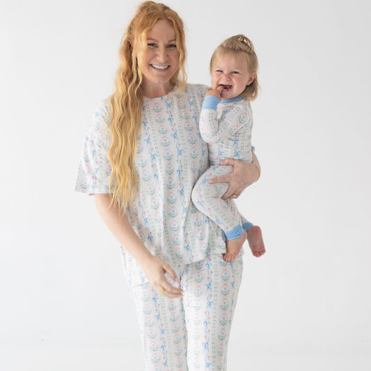 Woman and child wearing matching pajamas featuring dainty blue bow detailing on a white background