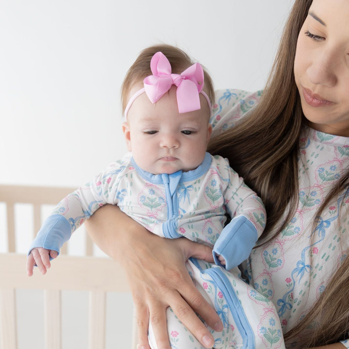 Woman holding a baby wearing matching blue floral with white background pajamas.