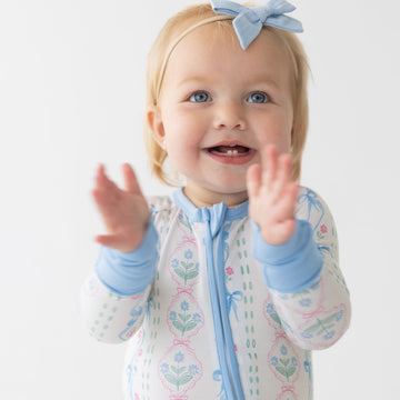 Baby in a floral romper with blue accents sitting on a white background