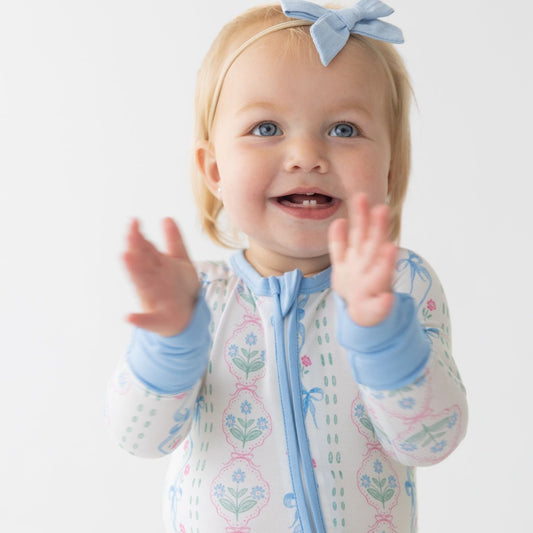 Baby in a floral romper with blue accents sitting on a white background