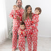 A family of five wearing matching red Christmas-themed pajamas with a Santa Claus, christmas tree, candy cane, teddy bear repeating pattern, standing together in front of a white wall and a small Christmas tree.