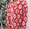 A young boy close up wearing a red long-sleeve pajama set with christmas trees, candy canes, Santa Claus pattern, standing barefoot in a room next to a flocked Christmas tree.