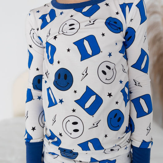 A toddler in a blue and white Duke University themed long sleeve two piece pajamas with smiley face and logo patterns.