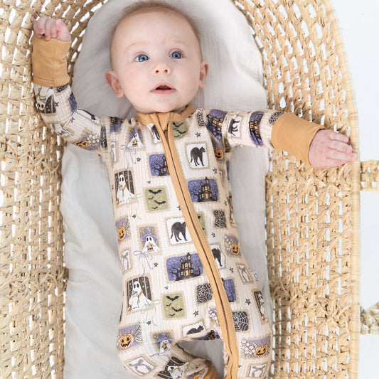 A baby lying on their back inside a woven rattan bassinet, wearing a beige base halloween-print featuring stamps of ghosts, black cat, bows, bats, spider webs, jack-o-lantern