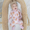 A baby lying in a woven straw Moses basket, wearing a pink and white striped gingerbread repeating print.