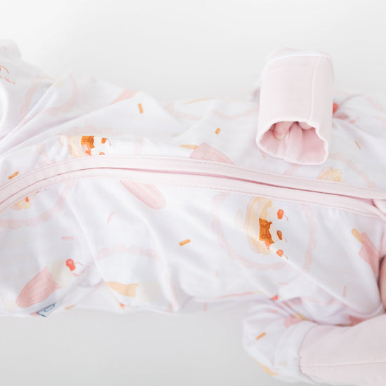 A sleeping newborn baby wearing a pink ice cream bar, ice cream sundae, ice cream cone pattern on a white background.