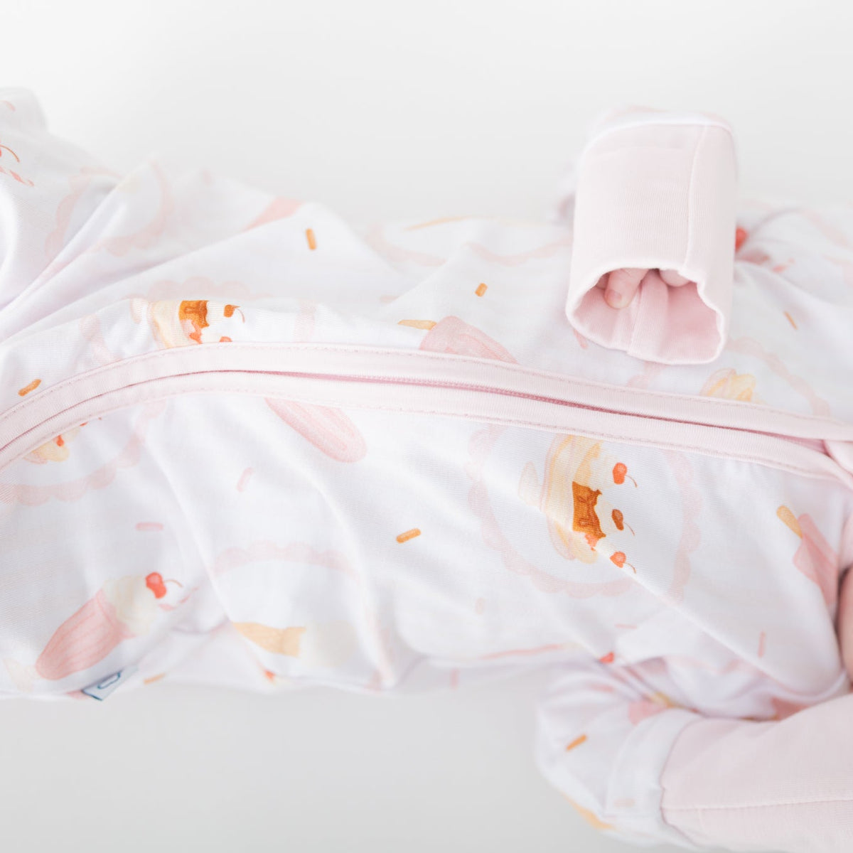 A sleeping newborn baby wearing a pink ice cream bar, ice cream sundae, ice cream cone pattern on a white background.