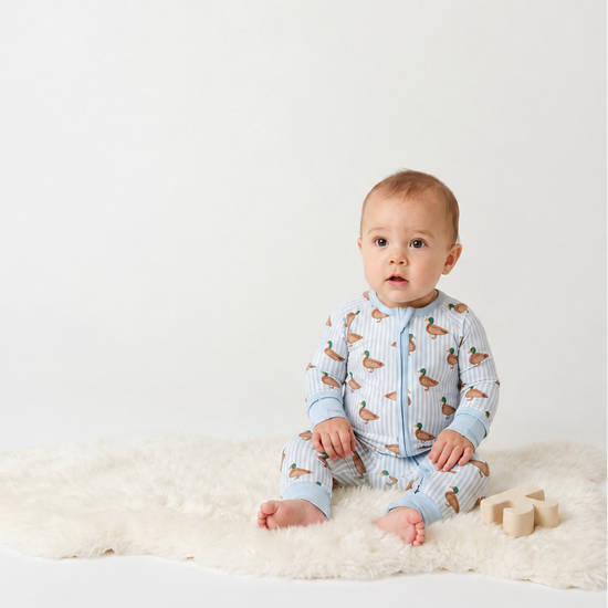 A baby wearing Monkeeroos mallards baby pjs sitting on a rug with a block next to him