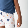 A child wearing white pinstriped shorts with a red and navy nautical print, paired with a blue t-shirt, shown from the side against a light gray background.