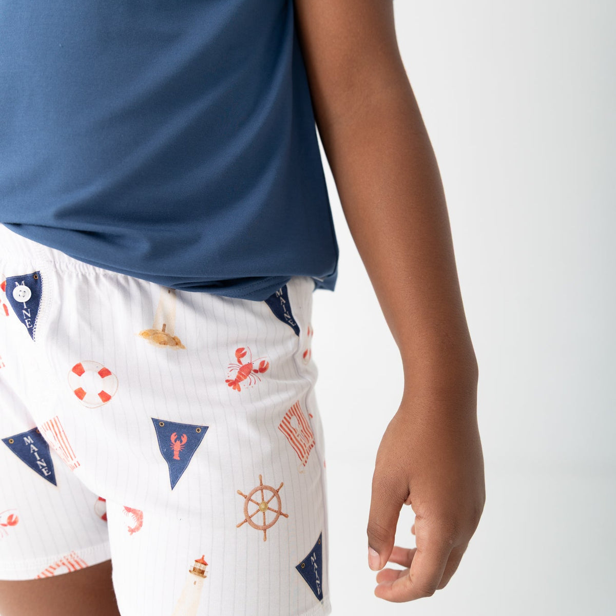 A child wearing white pinstriped shorts with a red and navy nautical print, paired with a blue t-shirt, shown from the side against a light gray background.