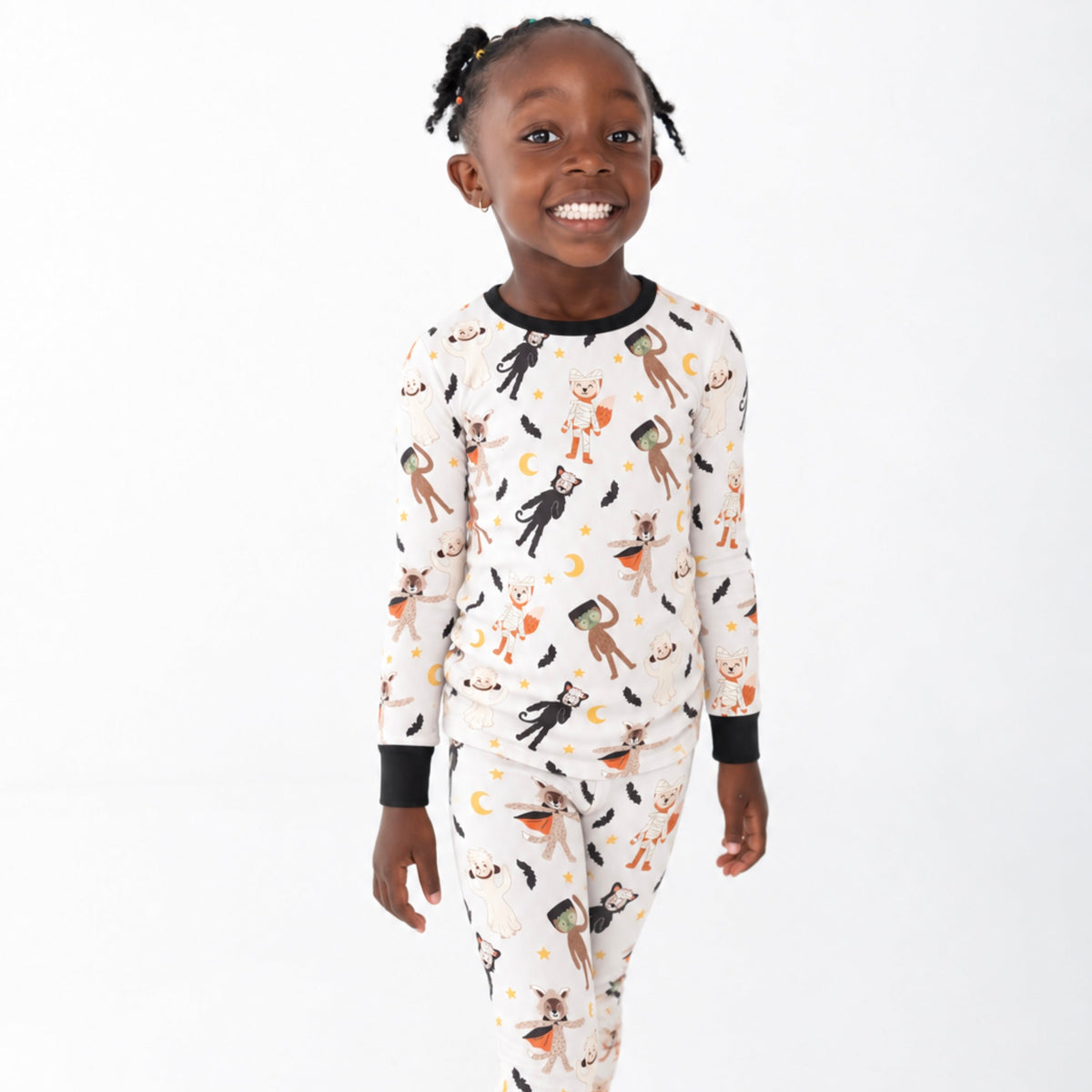A young child wearing a long-sleeve pajama set with a black and orange witch-themed print on a white background, standing against a plain white studio backdrop.