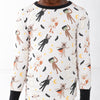A child wearing a long-sleeve and matching pajama set with an all-over Halloween-themed print of cartoon monsters, cats, dogs, bats, moons, and stars on an off-white background, with black trim at the collar and cuffs.
