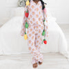 A young girl stands barefoot in a bright bedroom wearing a light pink pajama with a light pink and white stripes long-sleeve pajama set with an allover repeating gingerbread man print. 