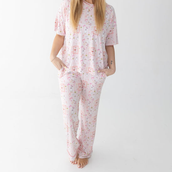 A woman stands against a white studio background wearing a matching short sleeve t-shirt and lounge pants featuring silly gooses, strawberries, hearts and bows. 
