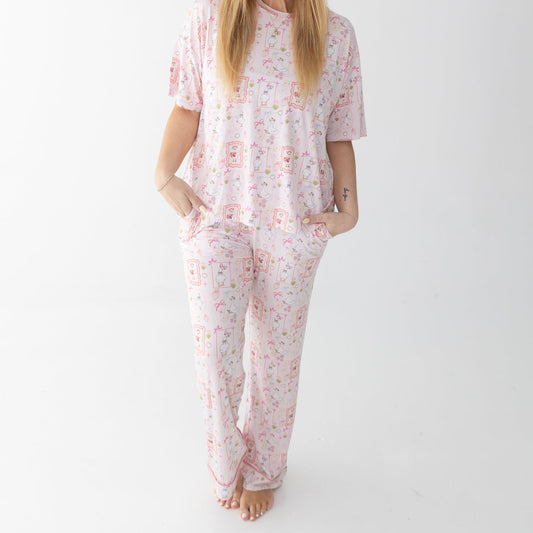 A woman stands against a white studio background wearing a matching short sleeve t-shirt and lounge pants featuring silly gooses, strawberries, hearts and bows. 