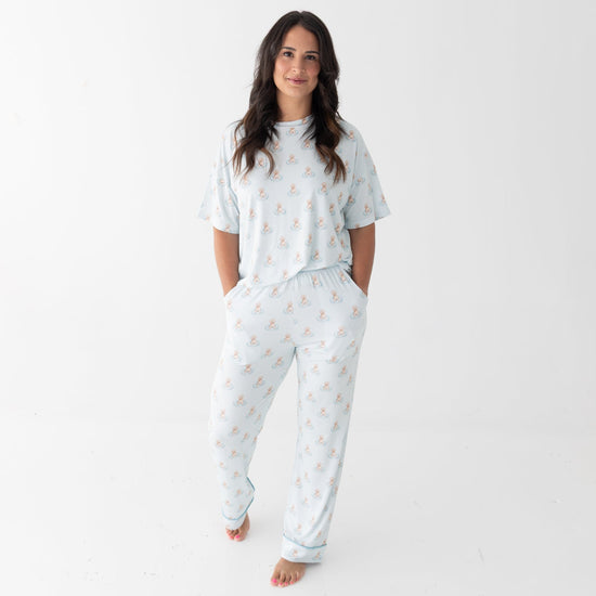 A woman modeling a matching two-piece pajama set consisting of a short-sleeve top and pants, both in a white base with a repeating a brown puppy in a blue floaty print