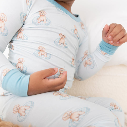 A close-up of a child wearing a light blue long-sleeve pajama set with a repeating a brown puppy in a blue floaty print
