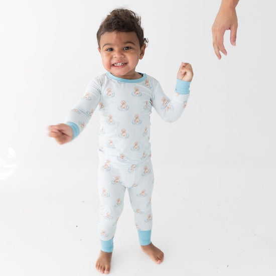 A toddler wearing a light blue and white long-sleeve pajama set with a repeating a brown puppy in a blue floaty print