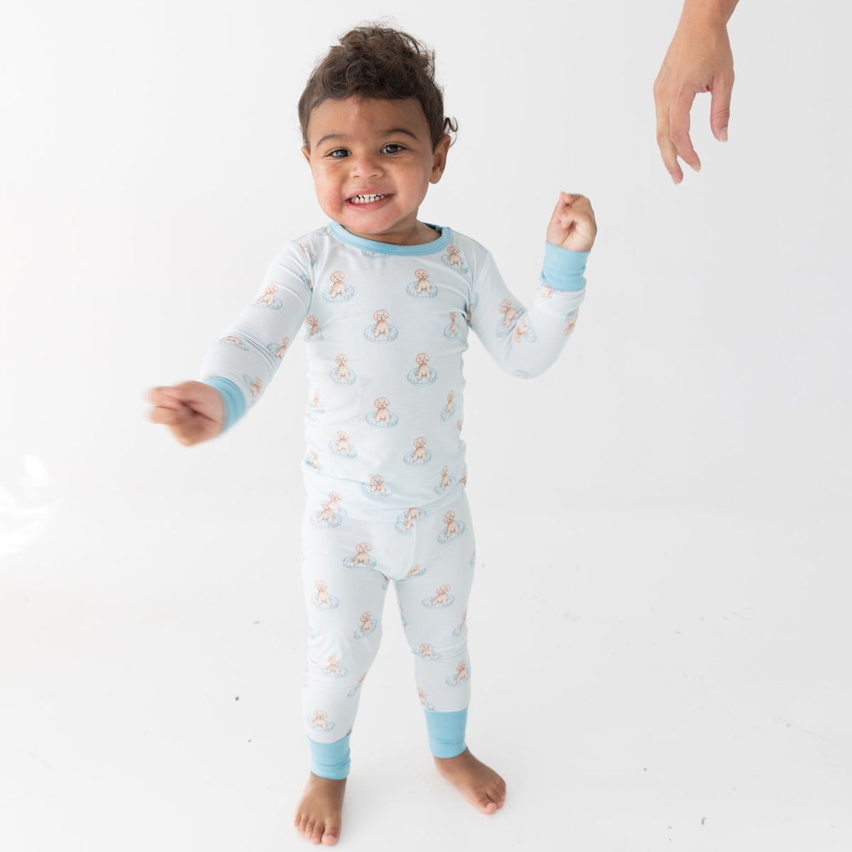 A toddler wearing a light blue and white long-sleeve pajama set with a repeating a brown puppy in a blue floaty print