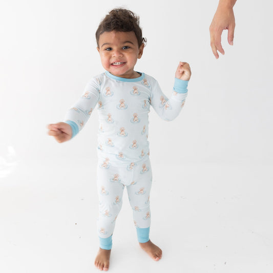 A toddler wearing a light blue and white long-sleeve pajama set with a repeating a brown puppy in a blue floaty print