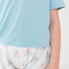 A close-up of a person wearing light blue t shirt with white shorts featuring a repeating a brown puppy in a blue floaty print