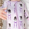 A close-up of a baby wearing a light purple and white striped romper with a purple zipper and an all-over print of black cats  and purple bows.
