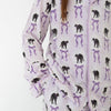 A close-up of a person wearing a matching pajama set with a white base, purple vertical stripes, and an all-over print of black cat silhouettes and purple bow-tie motifs.