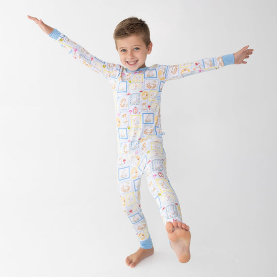 A young boy smiling and jumping in the air with his arms outstretched, wearing a long-sleeve two piece pajama blue and white patterned featuring silly gooses in a beach theme with watermelon, beach theme and palm trees.