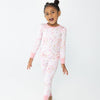 A young girl with her hair in a high bun is wearing a pink and white patterned two piece pajamas featuring silly gooses in a beach theme with strawberries, hearts and pink bows.