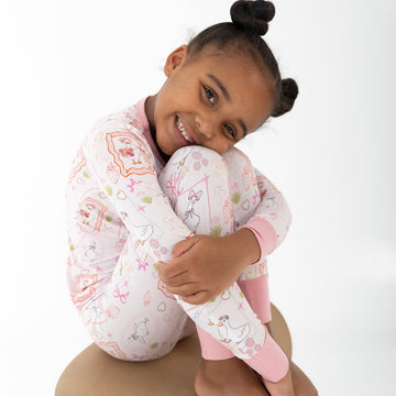 A young girl with her hair in a high bun is wearing a pink and white patterned two piece pajamas featuring silly gooses in a beach theme with strawberries, hearts and pink bows.
