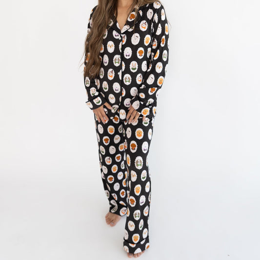A person wearing black pajama long-sleeve top with a white dog print pattern. The pajama top features a button-down front and a cozy collar, with a repeating pattern of dogs dressed up in costumes. 