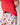 The image shows a close-up of a child wearing a bright red t-shirt and white shorts with a playful pattern. The shorts are decorated with illustrations of cows, chicken sandwiches, fries, soft drinks, and milkshakes, all in a whimsical, cartoon-like style. The child is slightly turned to the side, and their hand is resting on their hip. The background is a plain, light-colored wall.