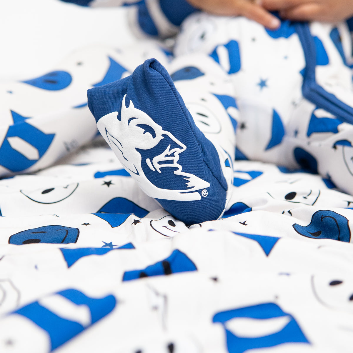 A baby in a blue and white Duke University themed romper with smiley face and logo patterns.