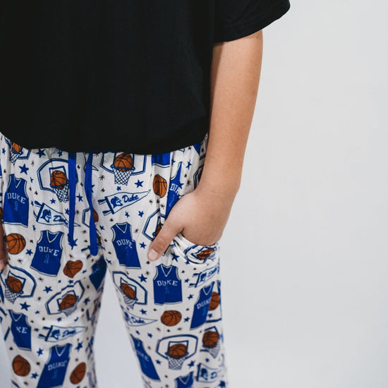 Close up photo of a short sleeve black t shirt, sports-themed design jogger pants with pockets on a white background featuring Duke University Basket ball, basket ball hoop, basket ball, Duke Jersey, Stars.