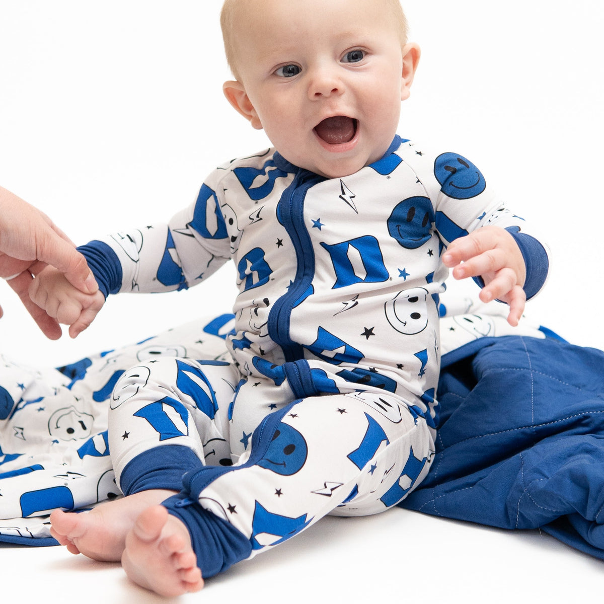 A baby in a blue and white Duke University themed romper with smiley face and logo patterns.