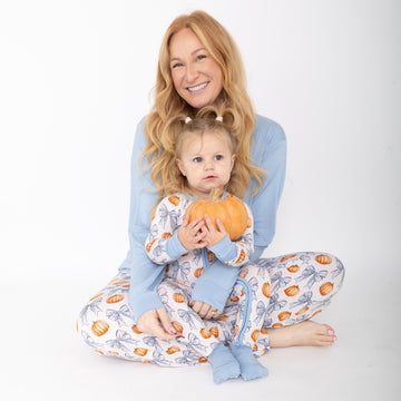 Mom and Baby wearing matching PJs. Mom has solid blue shirt and pants with pumpkins and blue bows repeating. Babu is wearing blue bow and pumpkin repeating print romper with blue accents