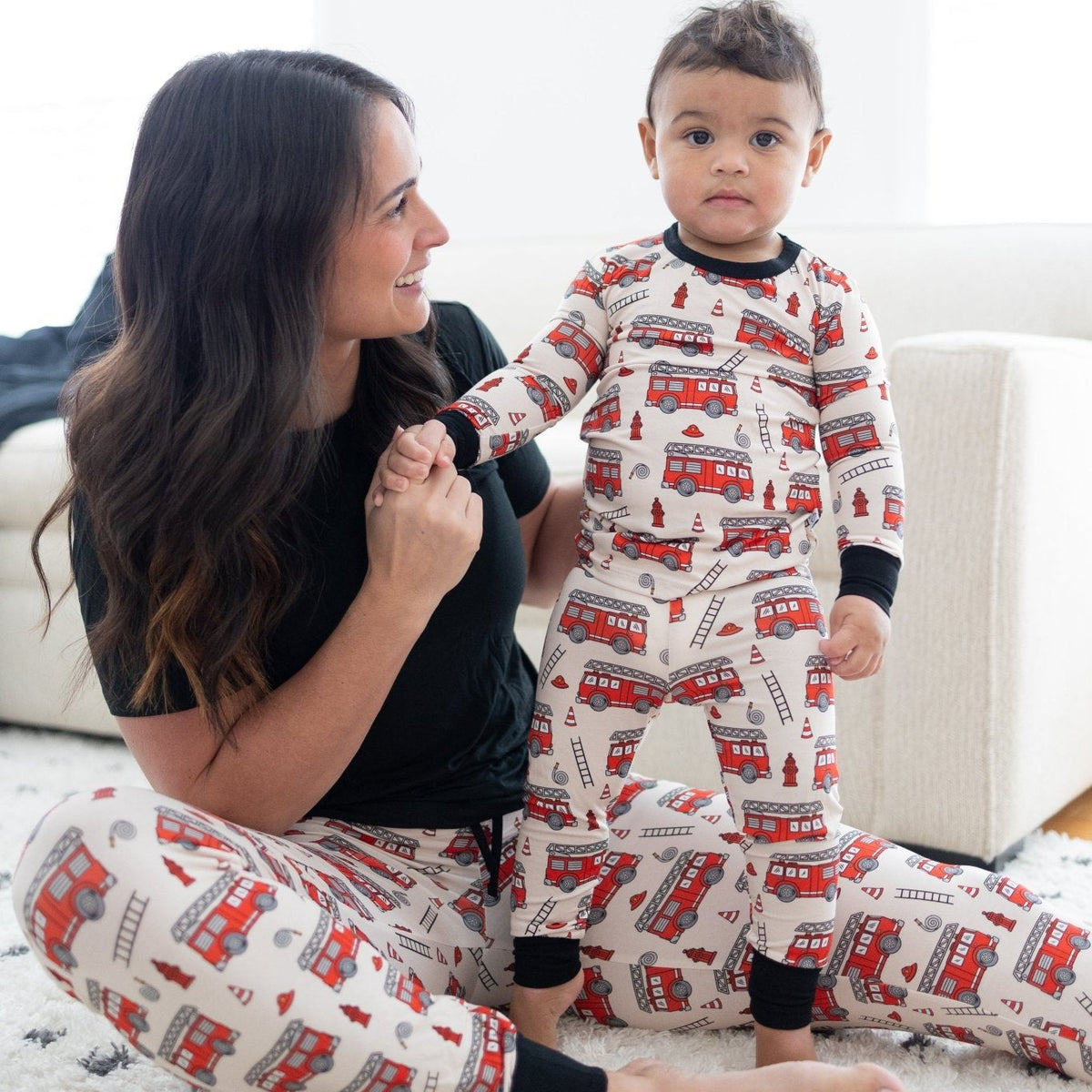 Woman and child wearing matching pajamas with fire truck pattern on a white couch.